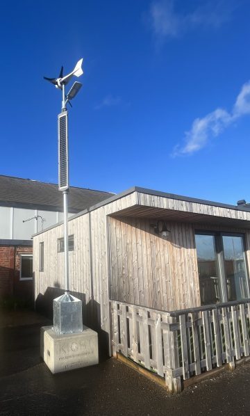 Wind turbine and solar panels mounted on lighting column with concrete base, placed next to office